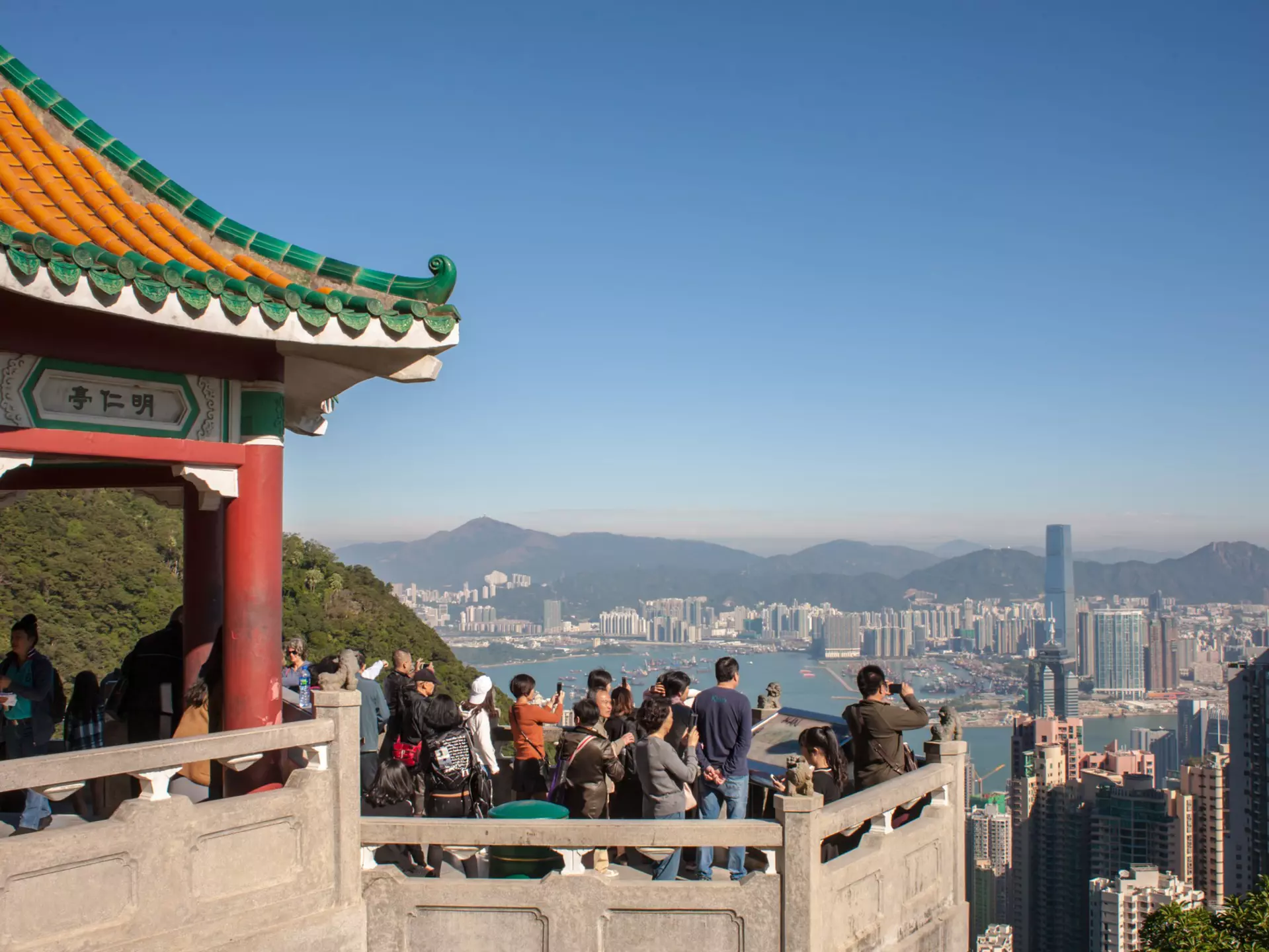 Tourists crowd at a Victoria Peak viewpoint looking out over the rooftops of Hong Kong.