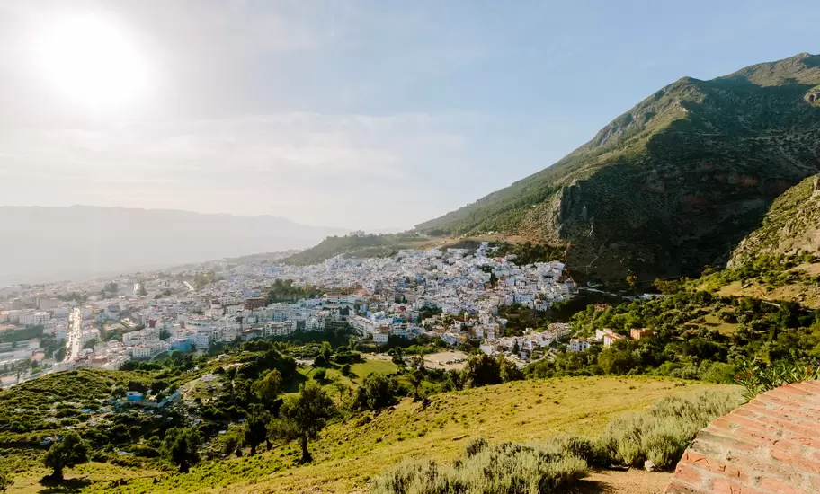 Blue-and-white town of Chefchaouen spread across a valley beneath green slopes of the Rif Mountains, Morocco