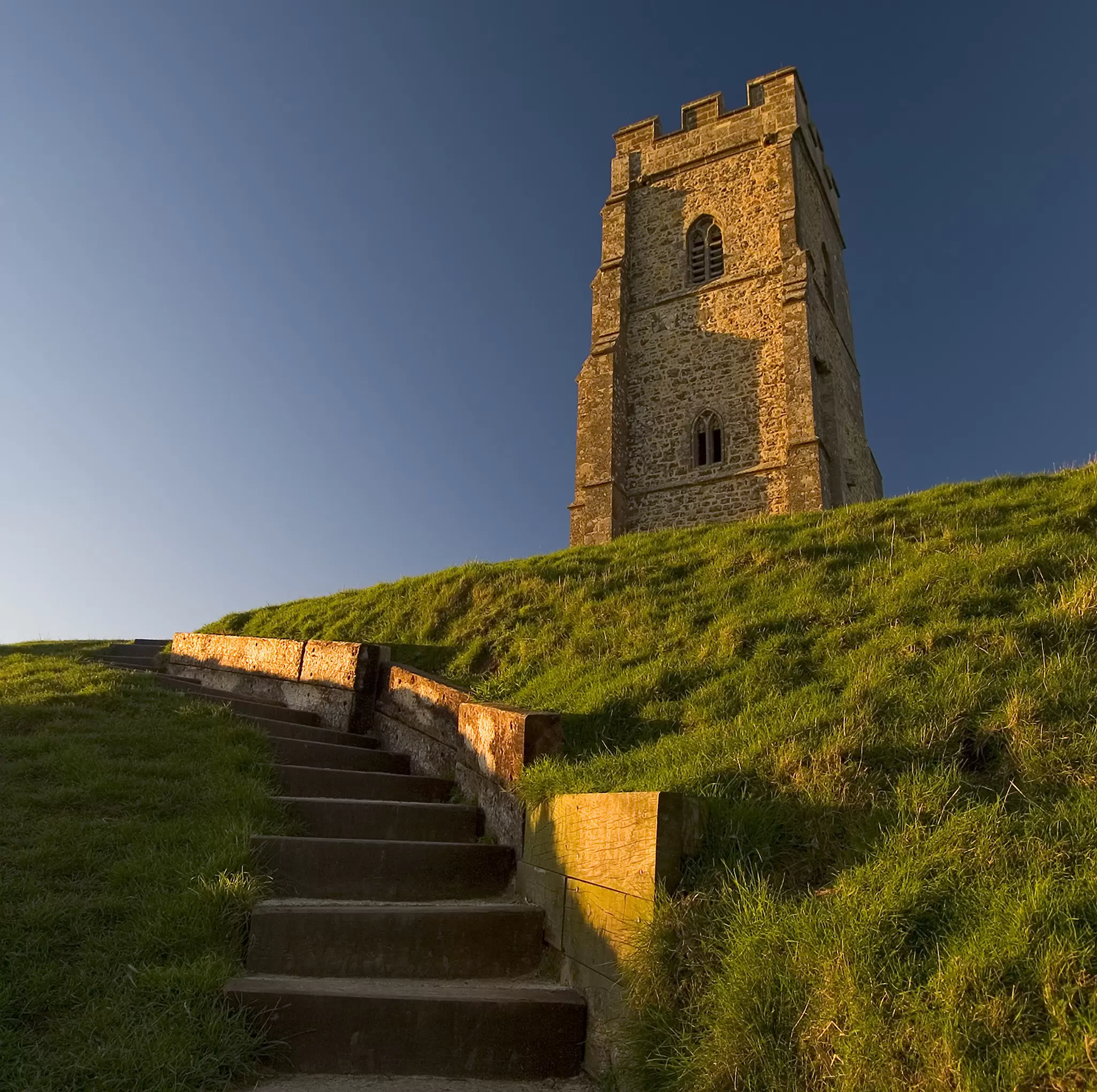 Steps in a steep grassy hillside. A large church-like tower stands at the top of the hill.