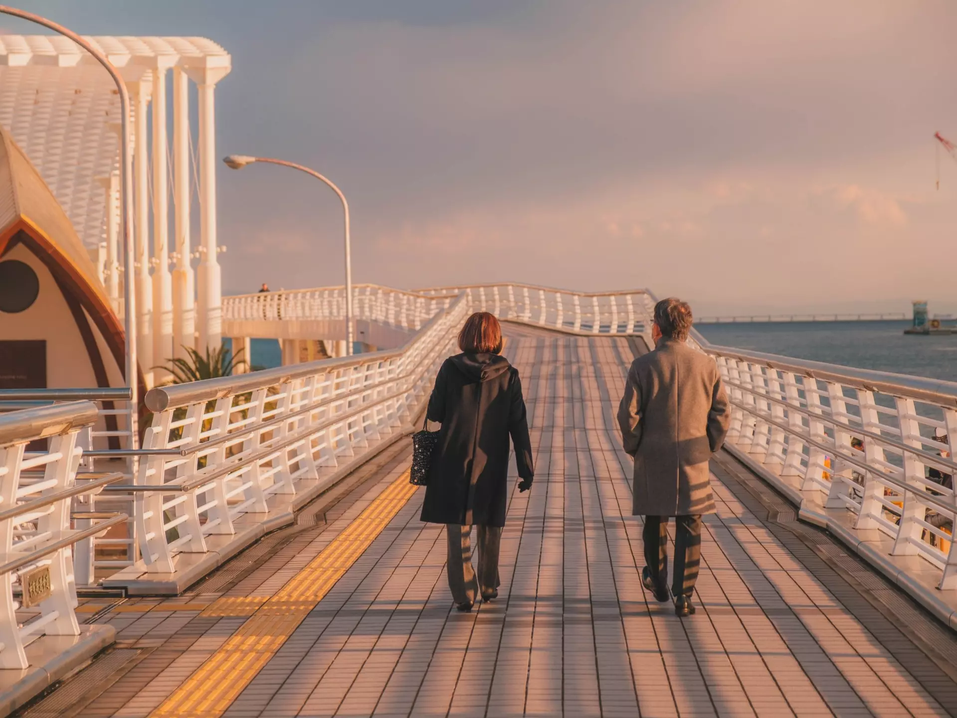 People walking on a boardwalk by water at sunset.