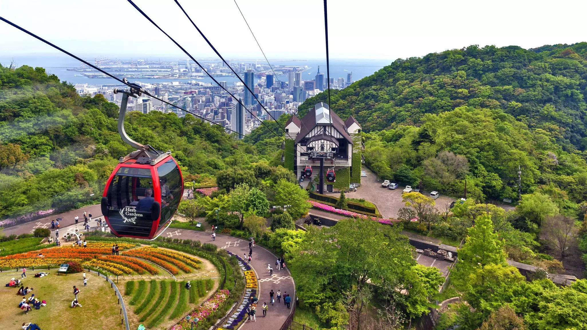 A red cable car glides over a landscaped garden.