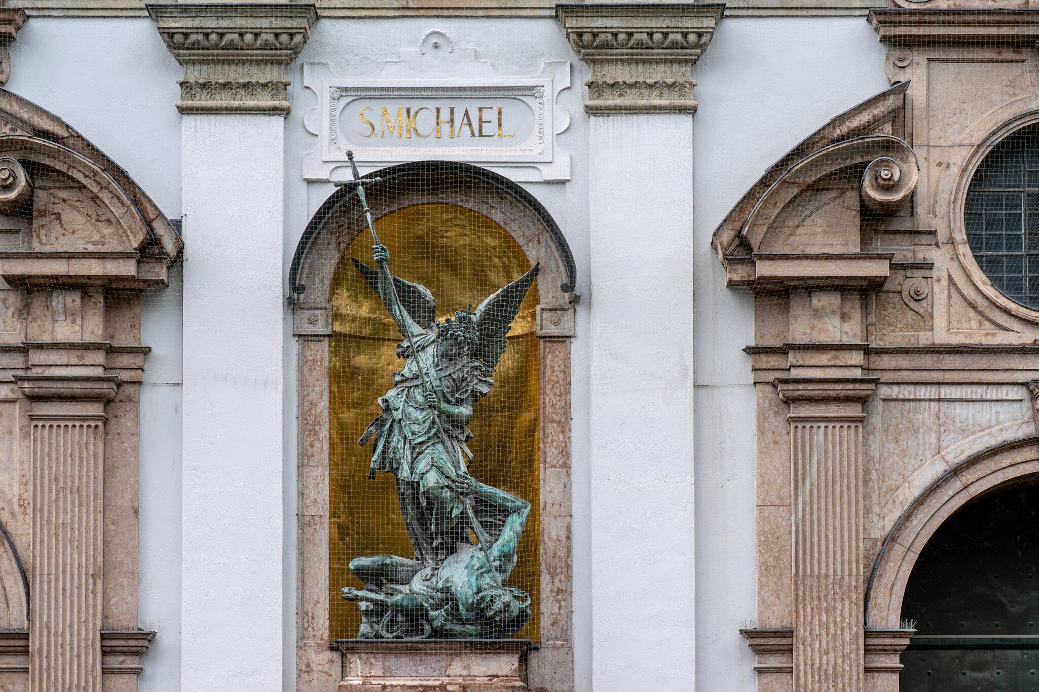 A bronze statue of Saint Michael slaying the dragon on the facade of St. Michael's Church in Munich, Germany.