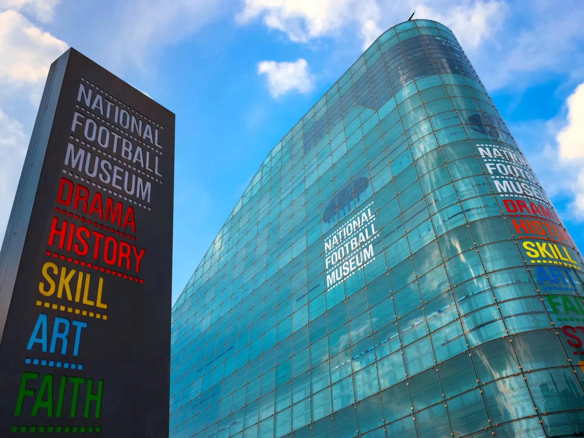 A tall curved glass building with a large sign outside it. The colorful writing says