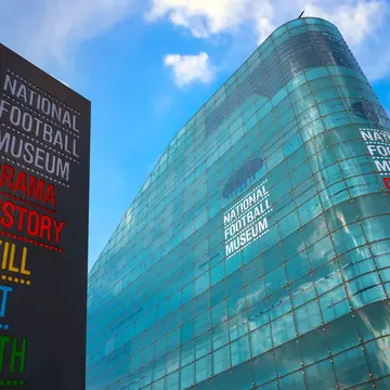A tall curved glass building with a large sign outside it. The colorful writing says