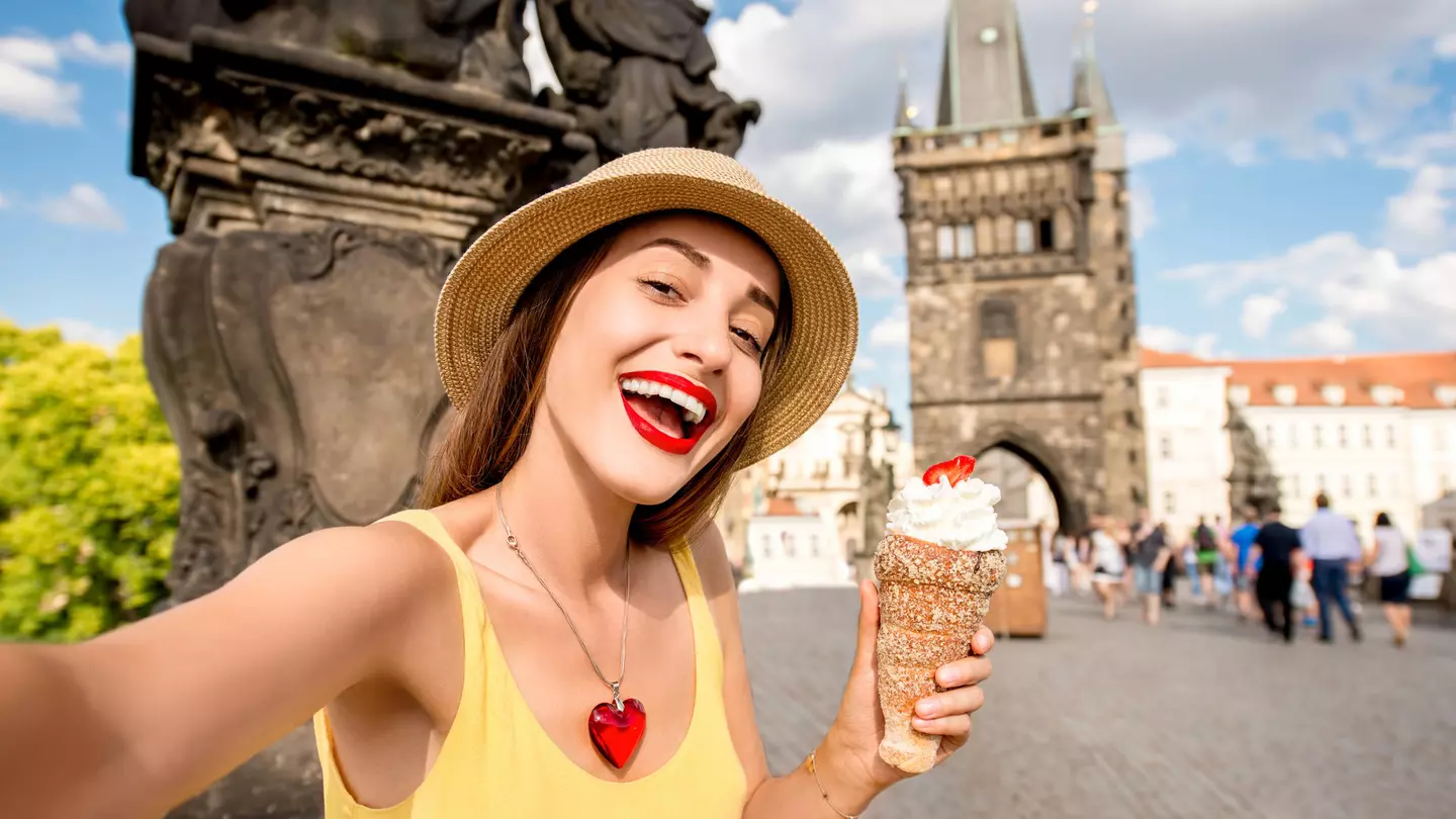 Three hands hold cinnamon rolls topped with ice cream with the Prague skyline in the backgroudn