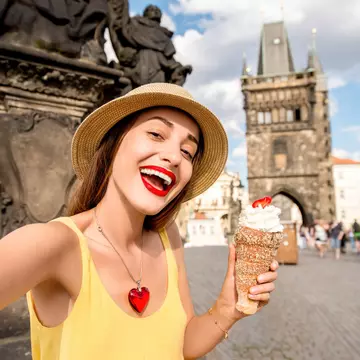 Three hands hold cinnamon rolls topped with ice cream with the Prague skyline in the backgroudn