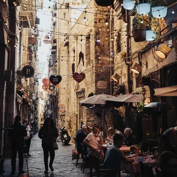 People sit at a sidewalk cafe in a shaded narrow alley.