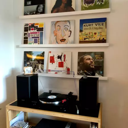 A record player and speakers are on a shelf; six albums are displayed on two shelves above.