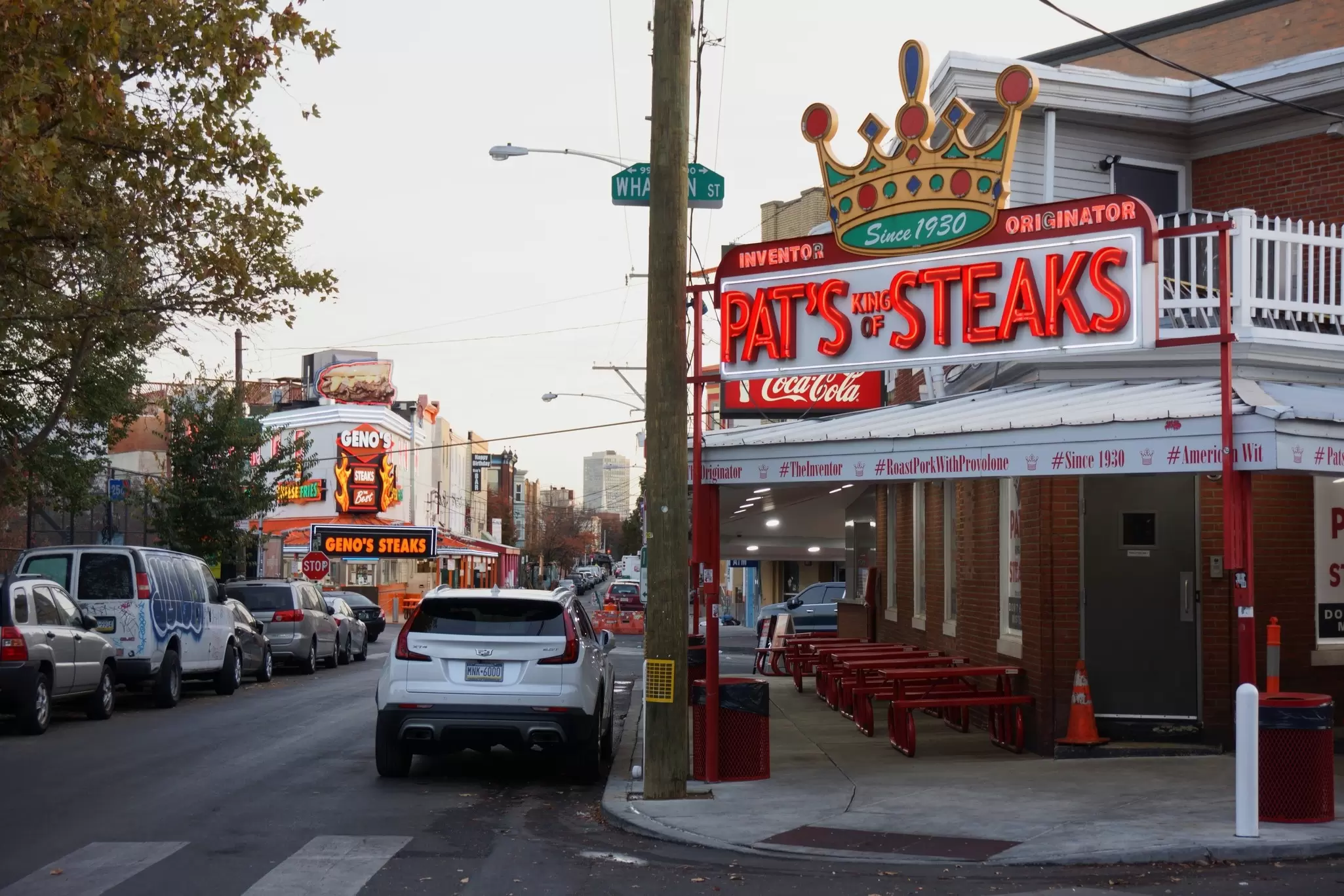 Street lined with cars and a building to the right with a red sign that says "Pat's Steaks".