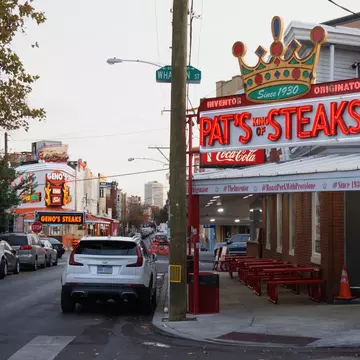 Street lined with cars and a building to the right with a red sign that says "Pat's Steaks".