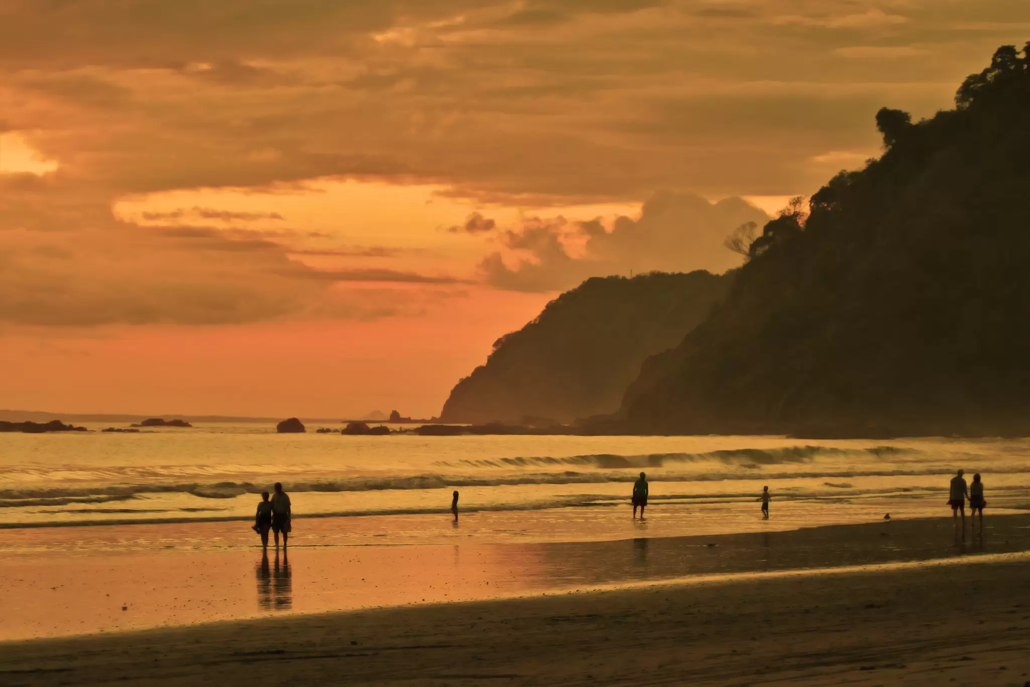 People walk along the surf at sunset on the beach in Costa Rica. 