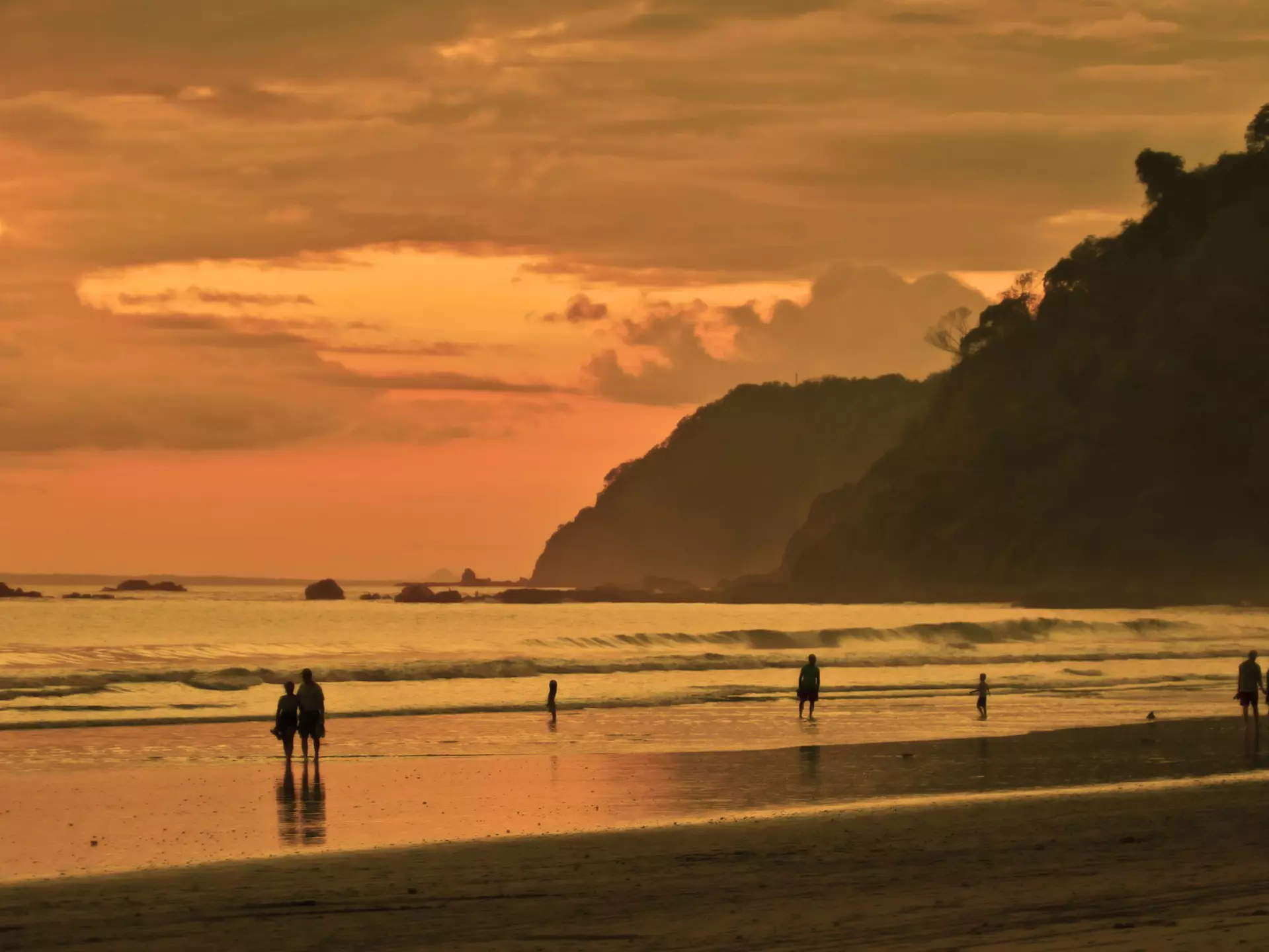 People walk along the surf at sunset on the beach in Costa Rica. 