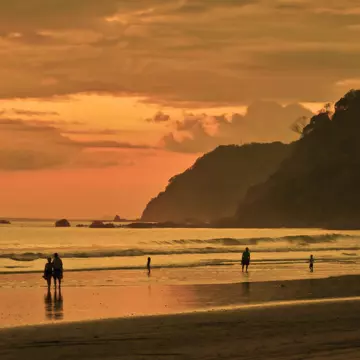 People walk along the surf at sunset on the beach in Costa Rica. 