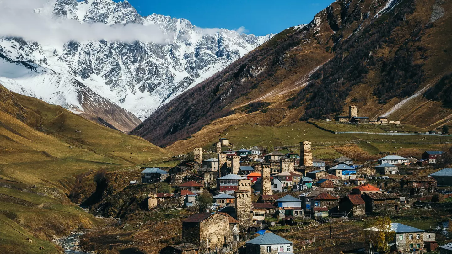 A remote mountain village surrounded by steep hills and mountains, with a variety of different buildings including unique stone towers.