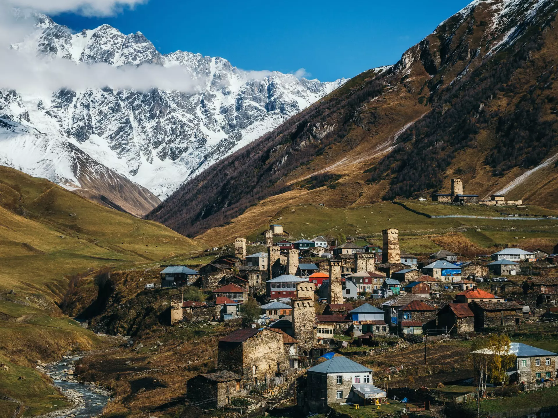 A remote mountain village surrounded by steep hills and mountains, with a variety of different buildings including unique stone towers.