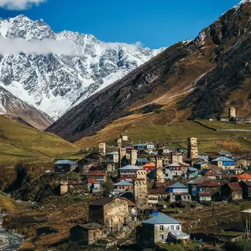 A remote mountain village surrounded by steep hills and mountains, with a variety of different buildings including unique stone towers.