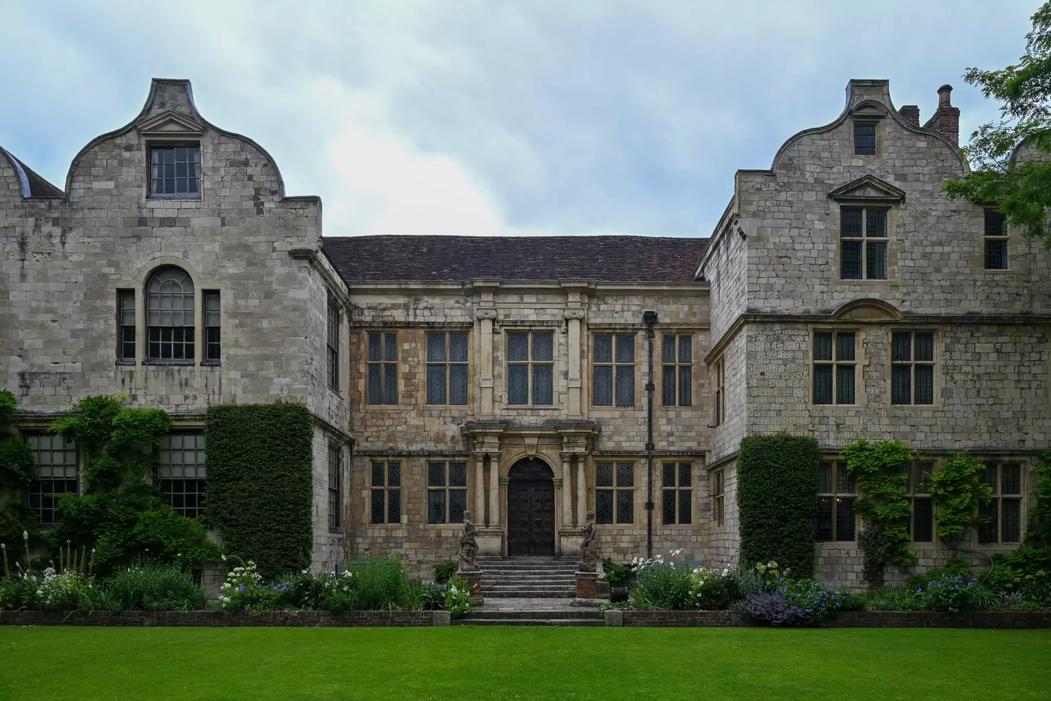 The front door and steps of a large stone house with green lawn in front on an overcast day.