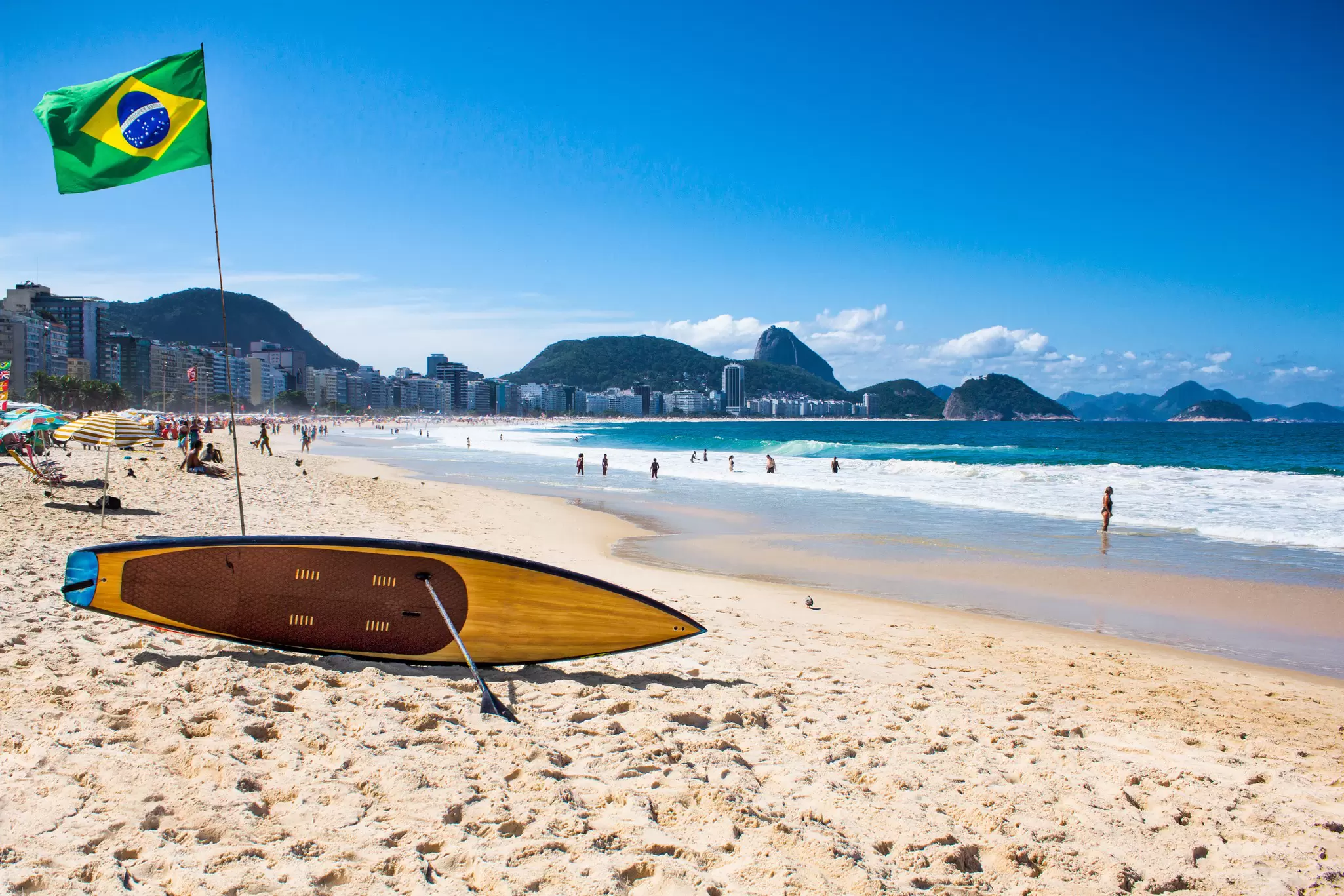 A Brazilian flag flies in the wind by a SUP board at Copacabana Beach in Rio de Janeiro, Brazil.