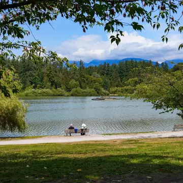 People relaxing on a bench on the shore of Lost Lagoon in Stanley Park, Vancouver, Canada.