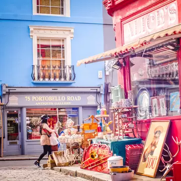 Shoppers walking past antique shops on a street with antiques on display and shopfronts in pastel colors