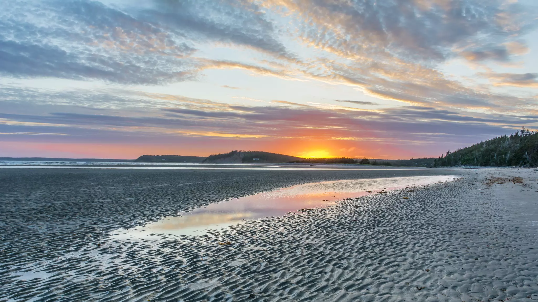 A sandy beach at low tide as the sun sets.