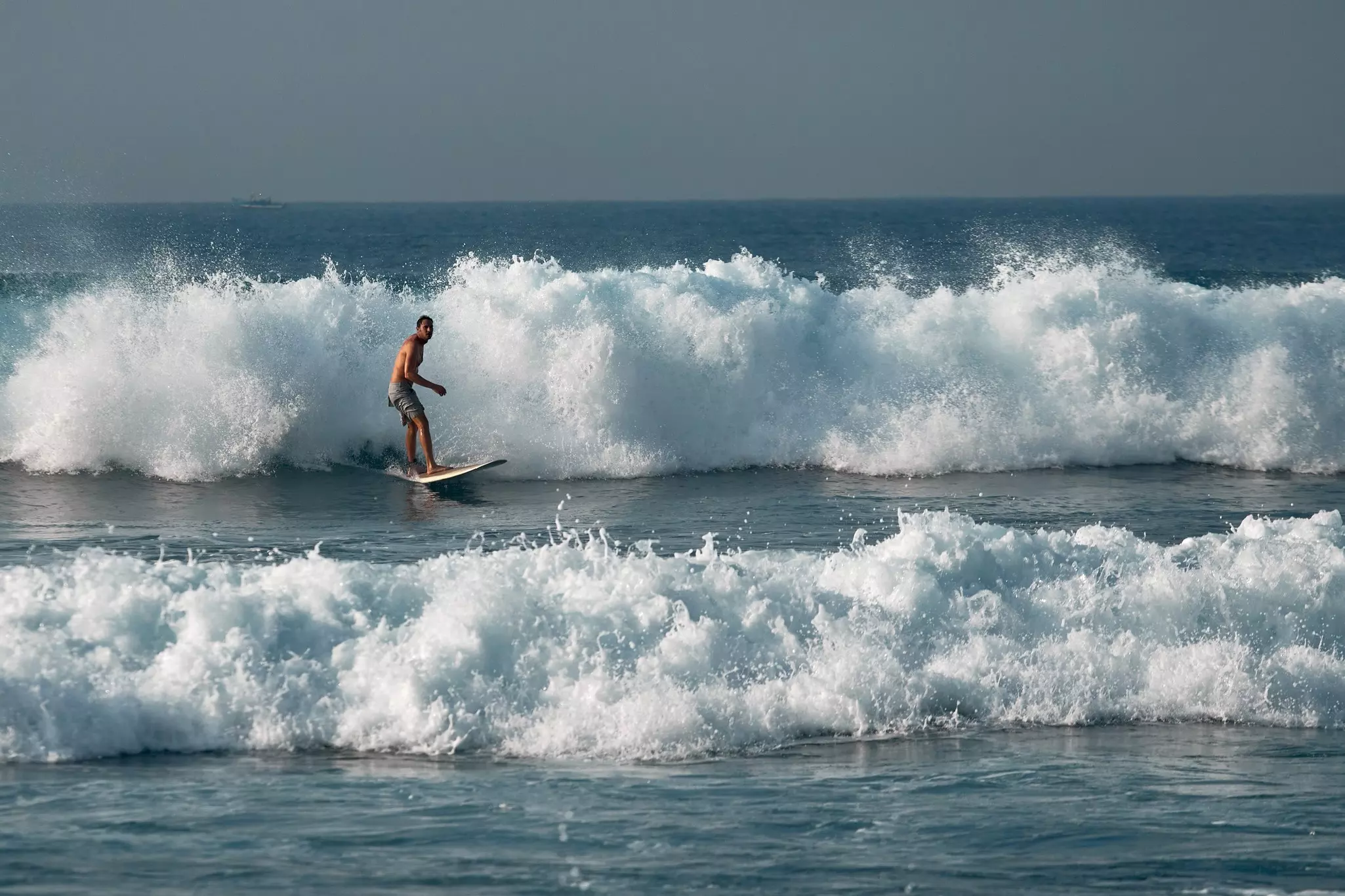 A male surfer stands up on his board as white-capped waves roll toward the shore.