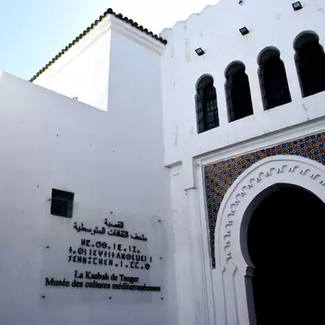 Whitewashed building with a tiled horseshoe archway and a trilingual museum sign.