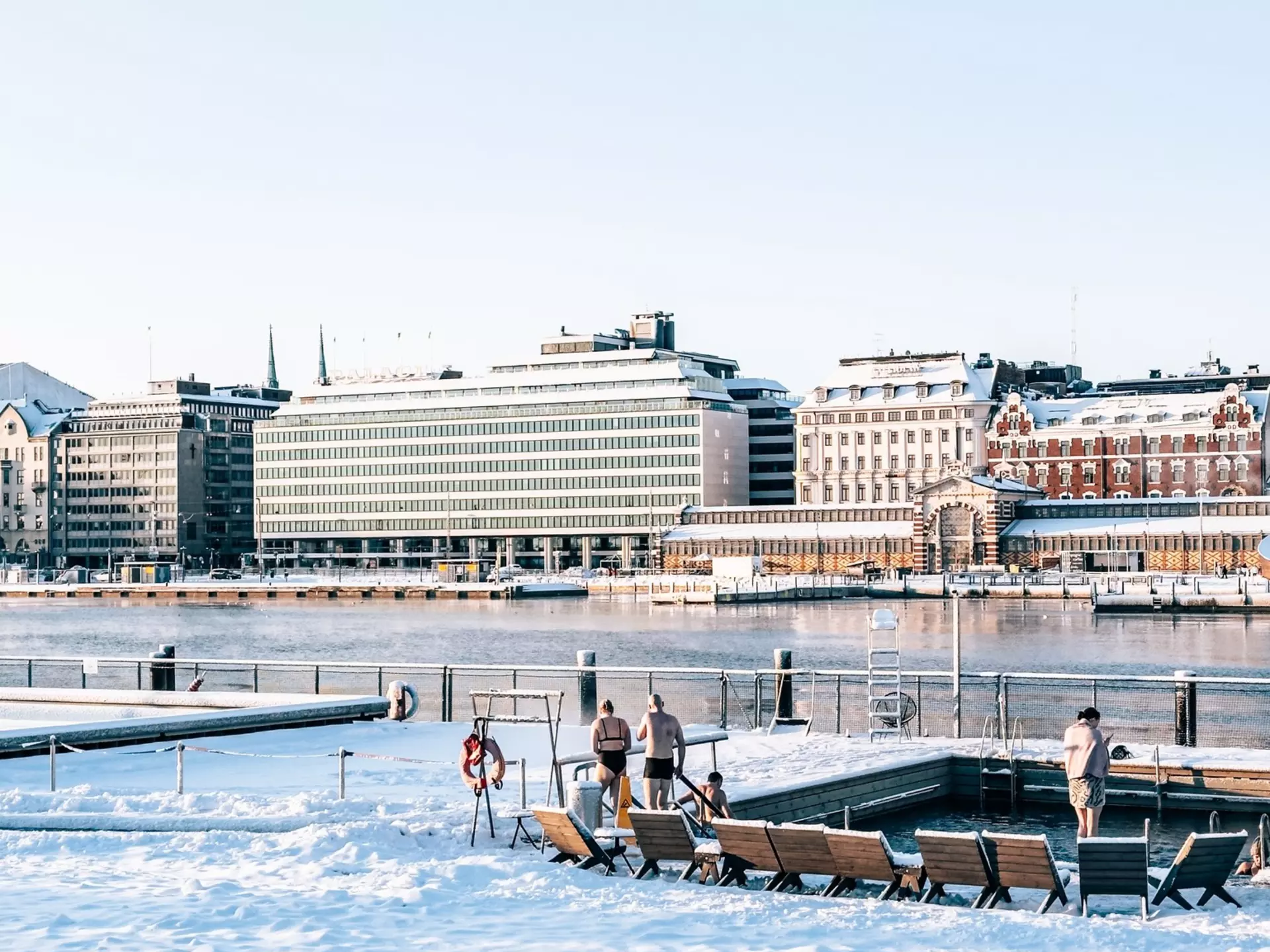 People at an outdoors city sauna that's surrounded by snow