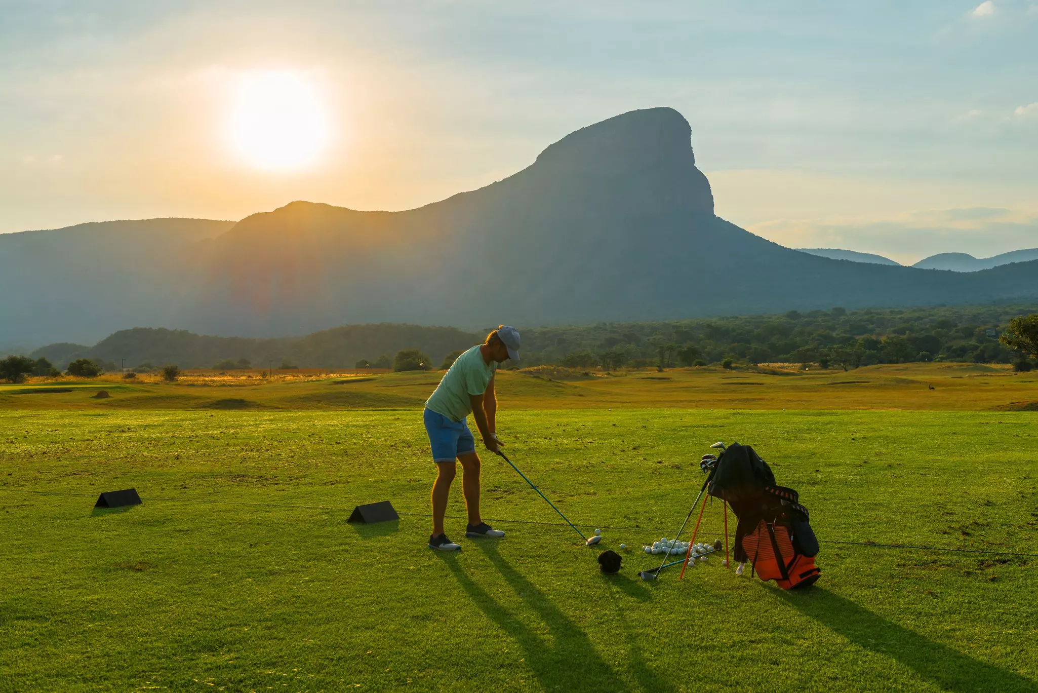 A young male caucasian adult playing golf inside the Entabeni Game Reserve at sunset with a view over the Hanglip or Hanging Lip mountain peak, Limpopo Province, South Africa.