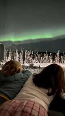 Two children leaning against a window looking at a snowy landscape in Fairbanks, Alaska, with greenish northern lights on the horizon.