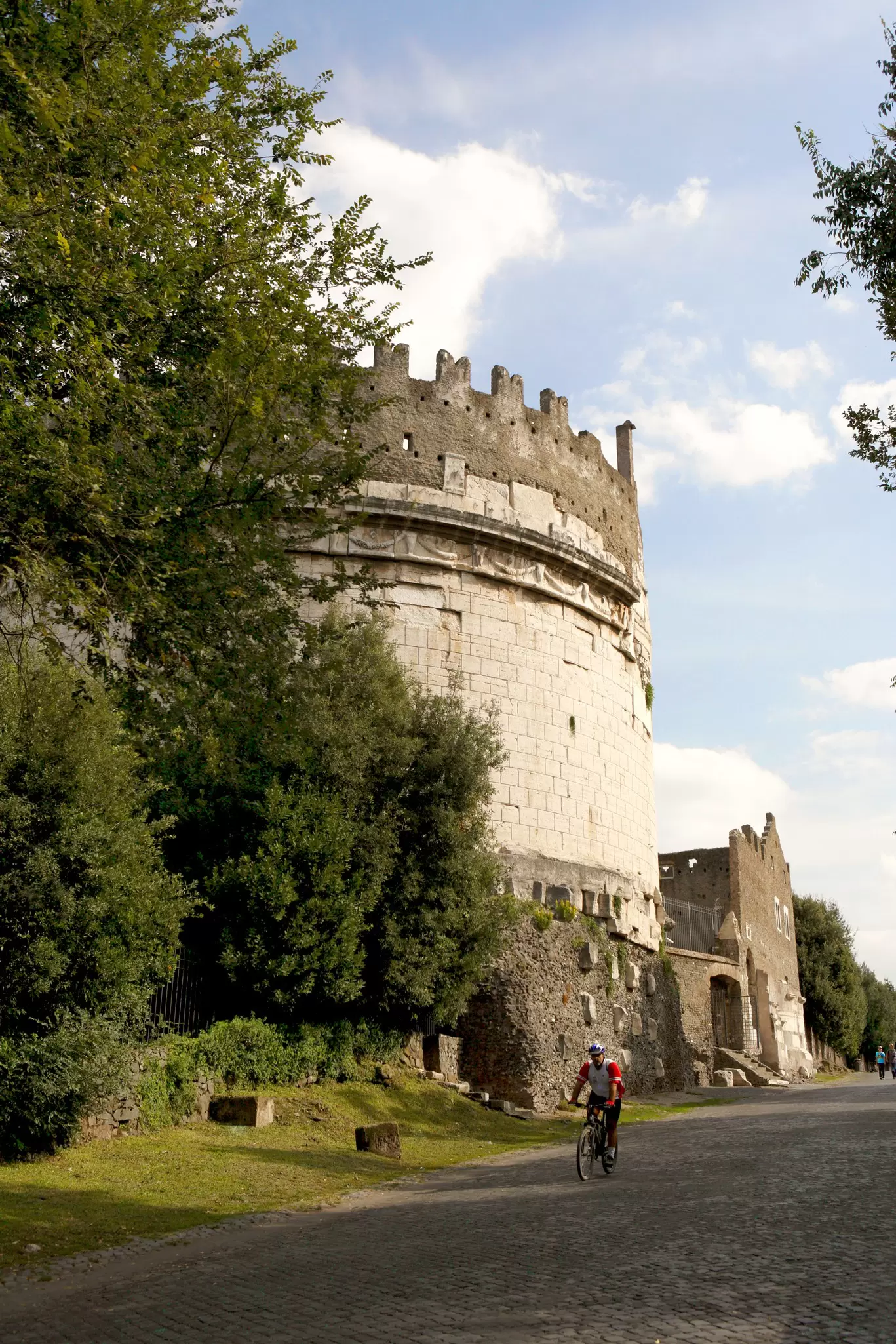Cyclist riding past the Mausoleo di Cecilia Metella on Via Appia Antica in Rome, Italy.