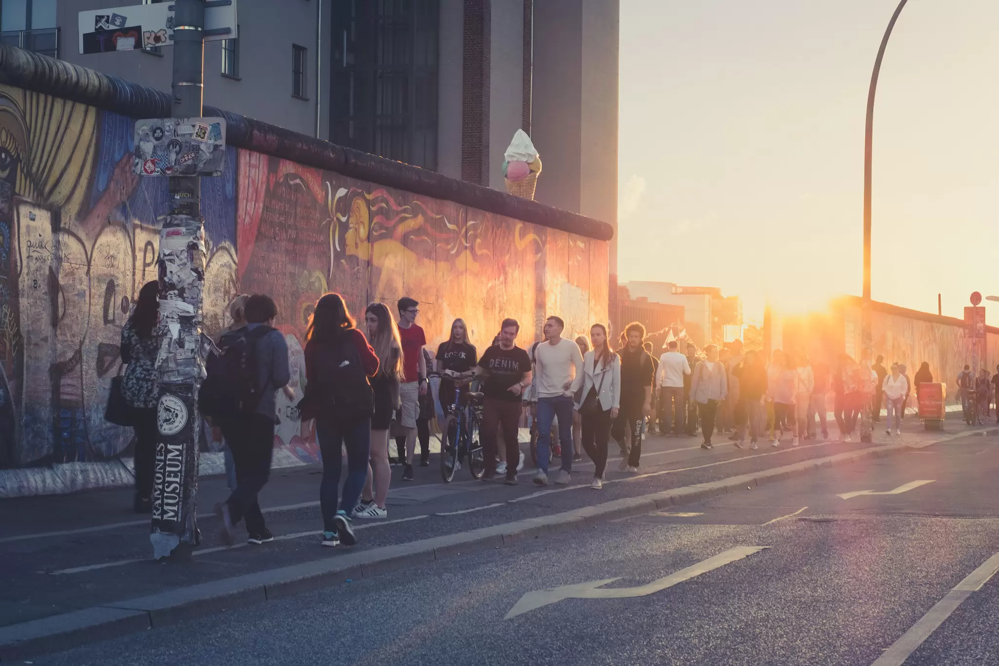 Young people walk beside the East Side Gallery on a summer evening with the sun setting in the background.