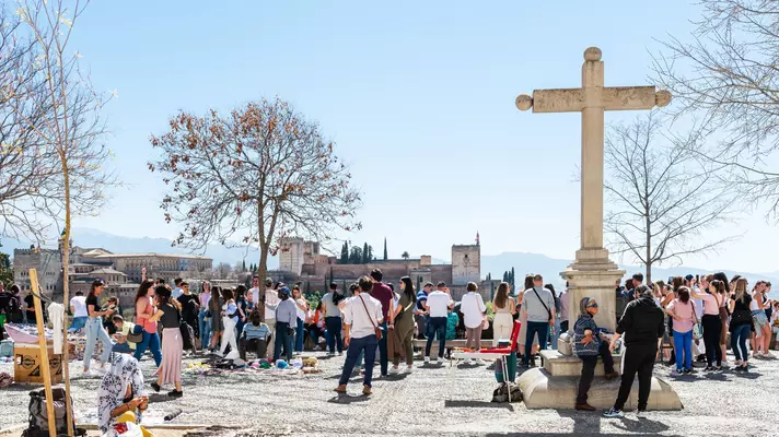 Crowded Mirador San Nicolás with tourists gathered around a viewpoint overlooking Granada