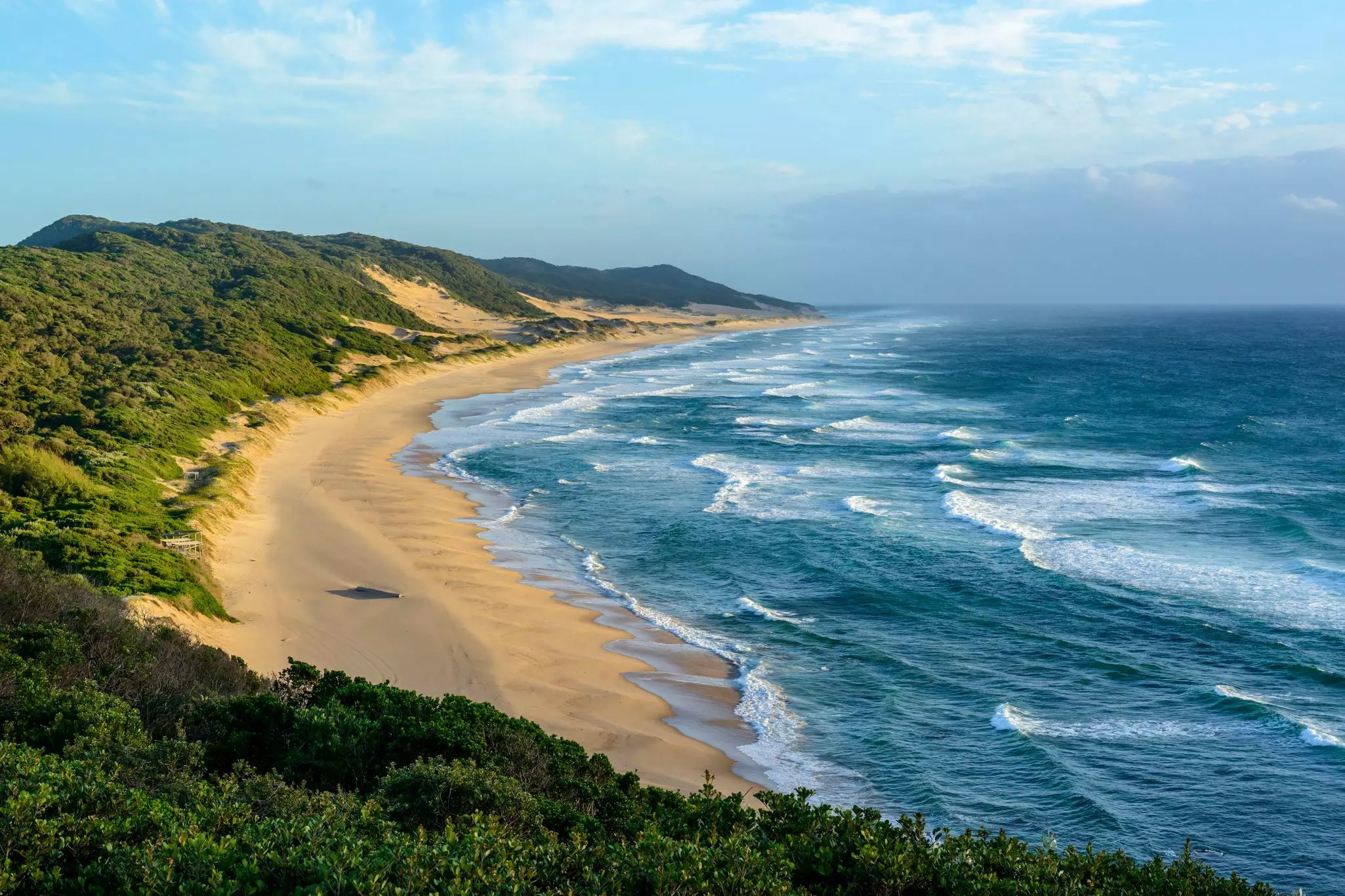 Waves hit the golden sands of a wild, sand dune-backed beach.