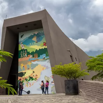 A tall slanted concrete portal frames a painted mural of mountains, farms and coast, with people below