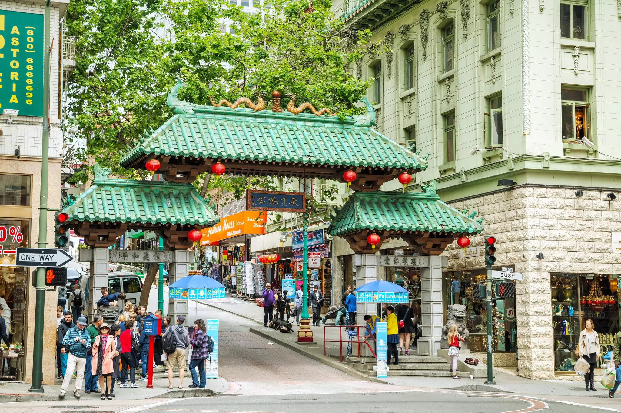 Green gateway roof entrance to Chinatown in San Francisco, with red lanterns hanging from it. People are standing on the sidewalks nearby.