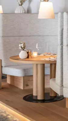 A gray upholstered booth with a blond wood table.