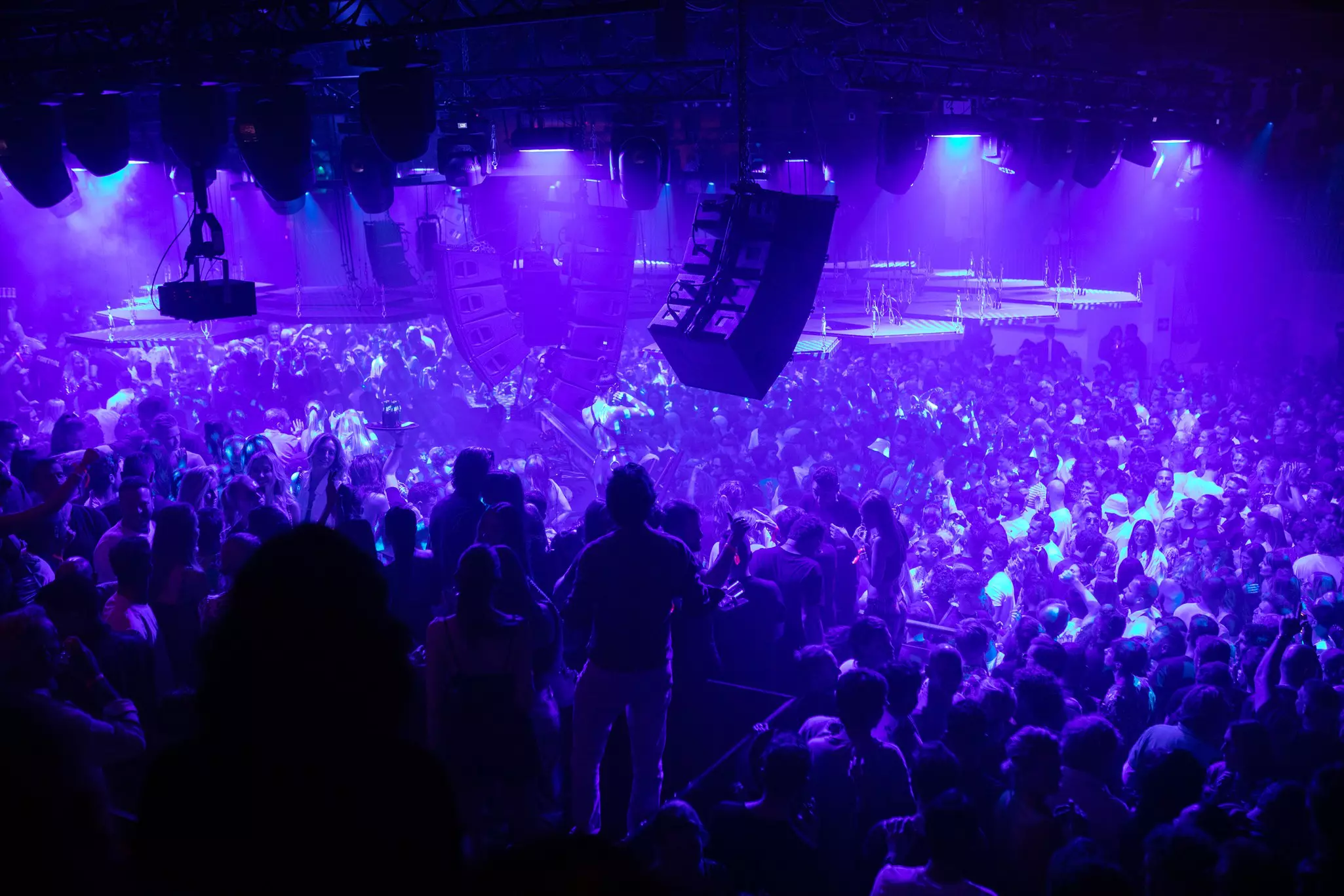 Purple lights illuminate thousands of dancers at a huge nightclub.
