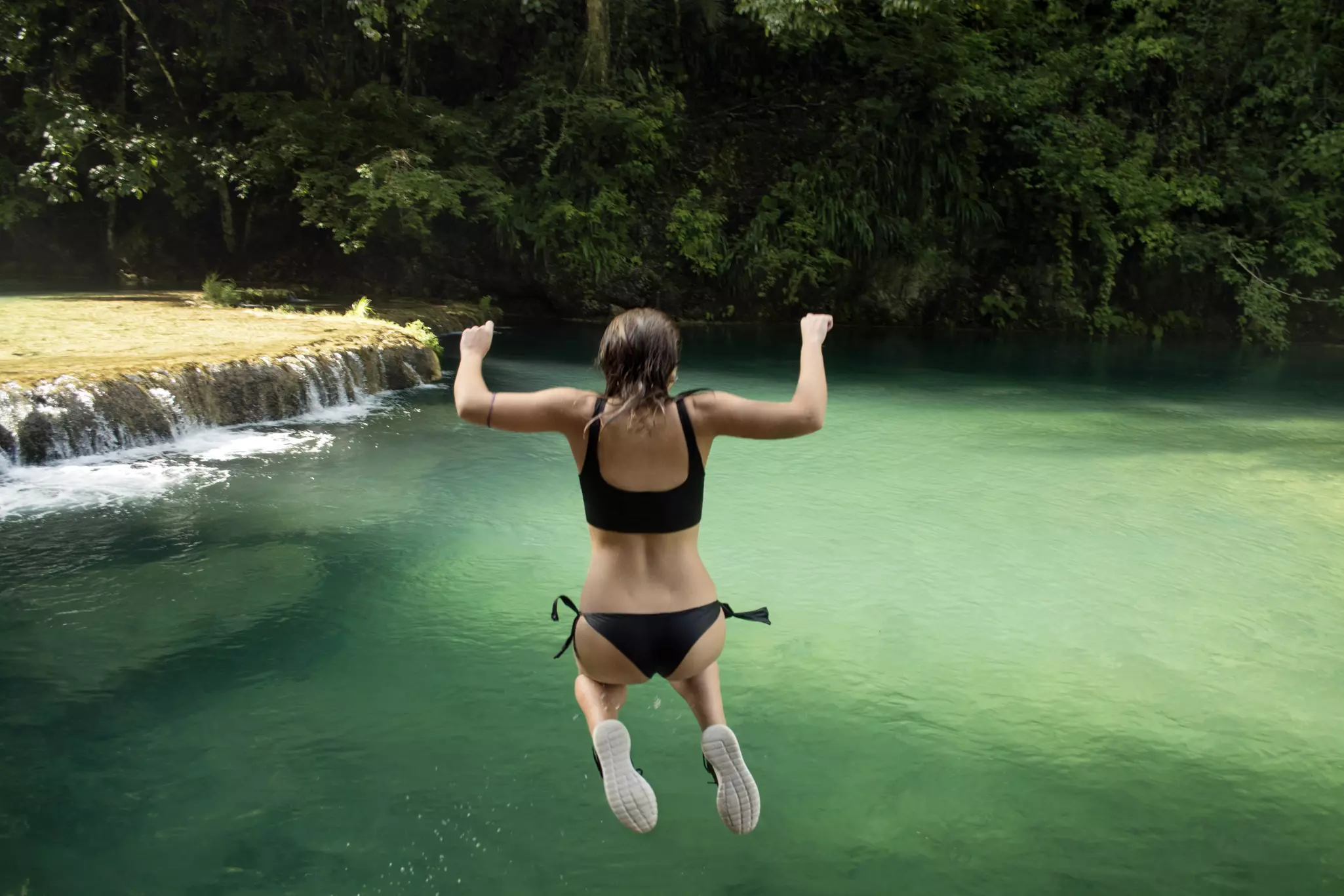 Rear view of woman jumping into a pool against trees in Semuc Champey, Guatemala