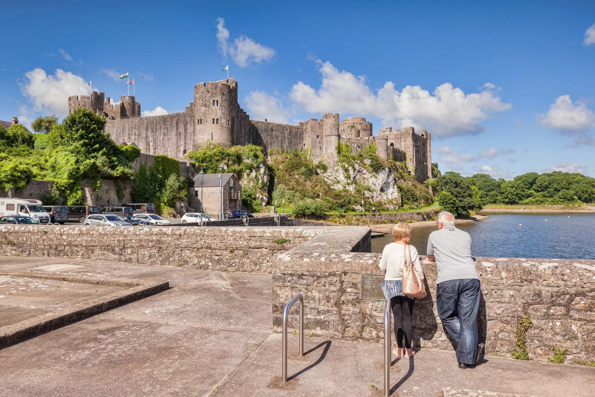 A couple looking across the water to Pembroke Castle, Pembrokeshire, Wales.