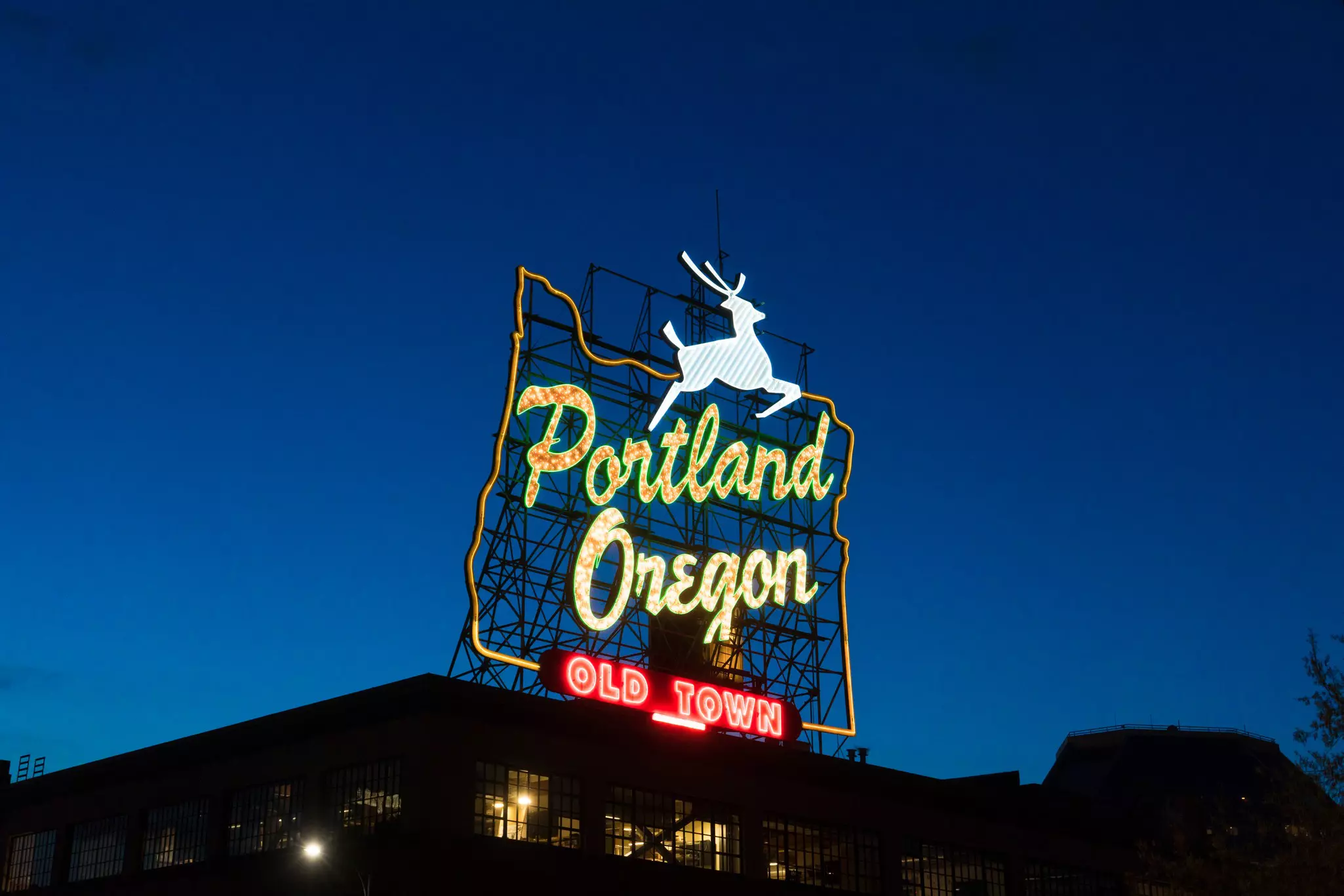 Neon sign in the shape of Oregon with a white stag jumping up top and the words "Portland, Oregon, Old Town" at night.