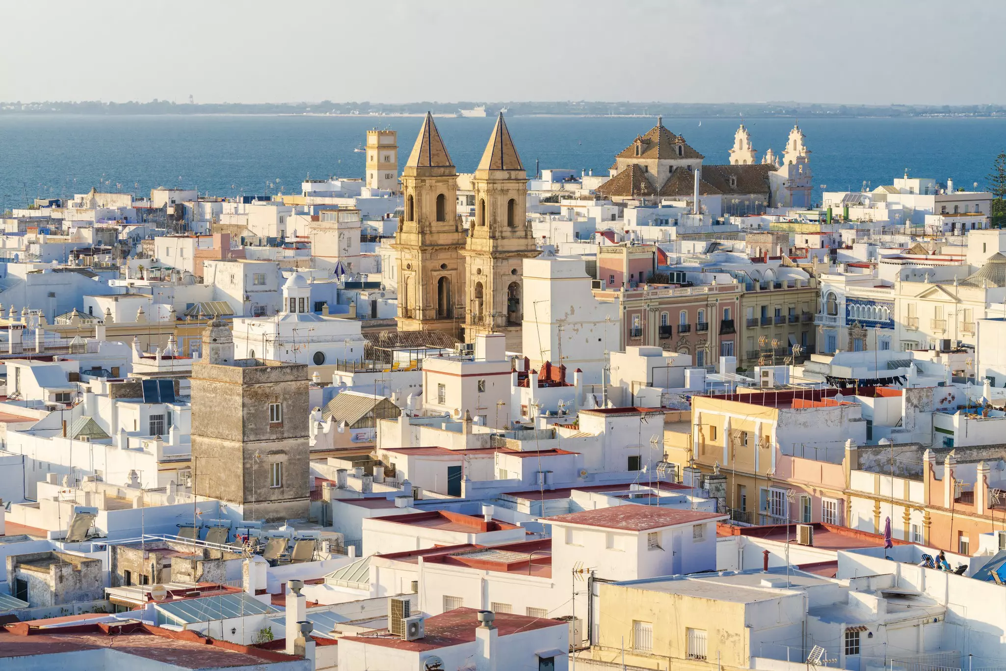 View over the rooftops of a low-rise ocean-side city with several tall church towers.