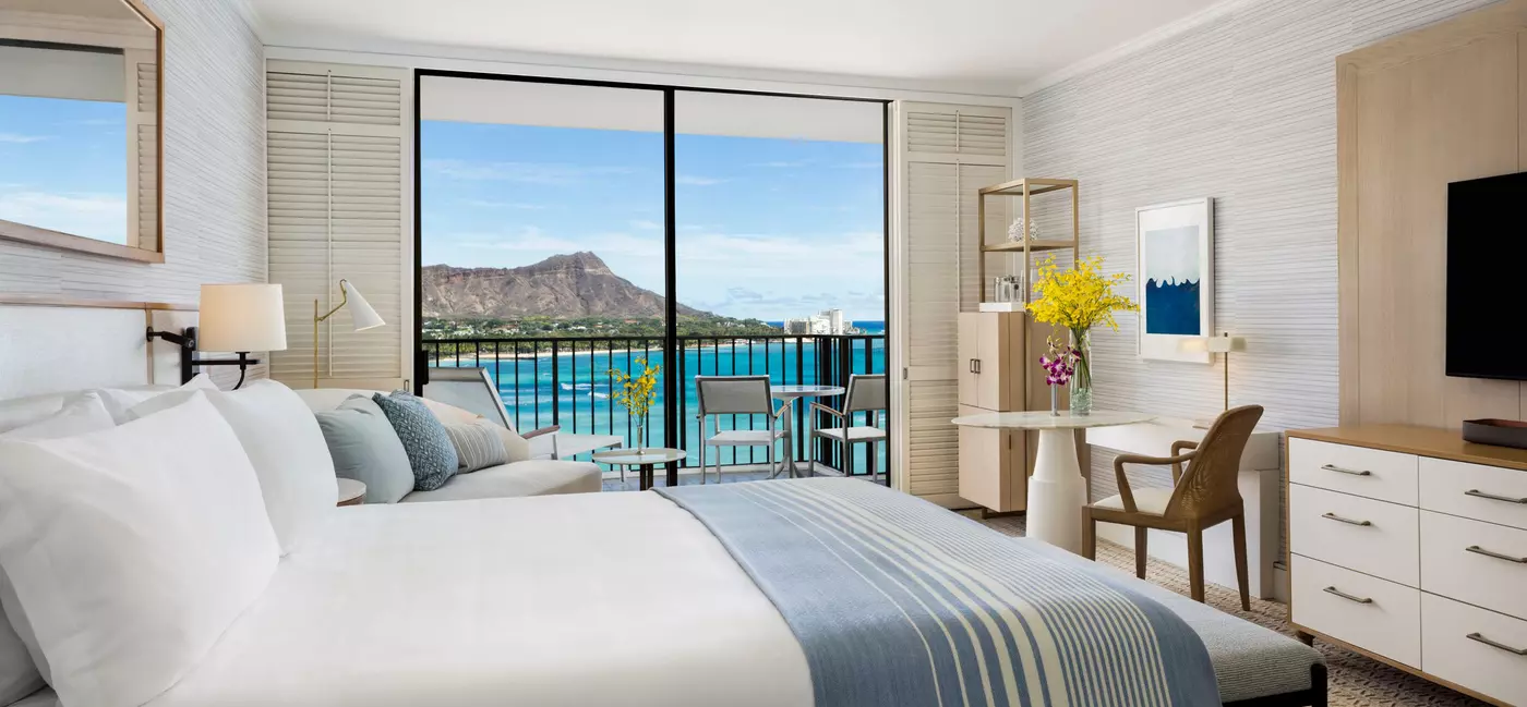 A large bed in a hotel suite with ocean views from the balcony.