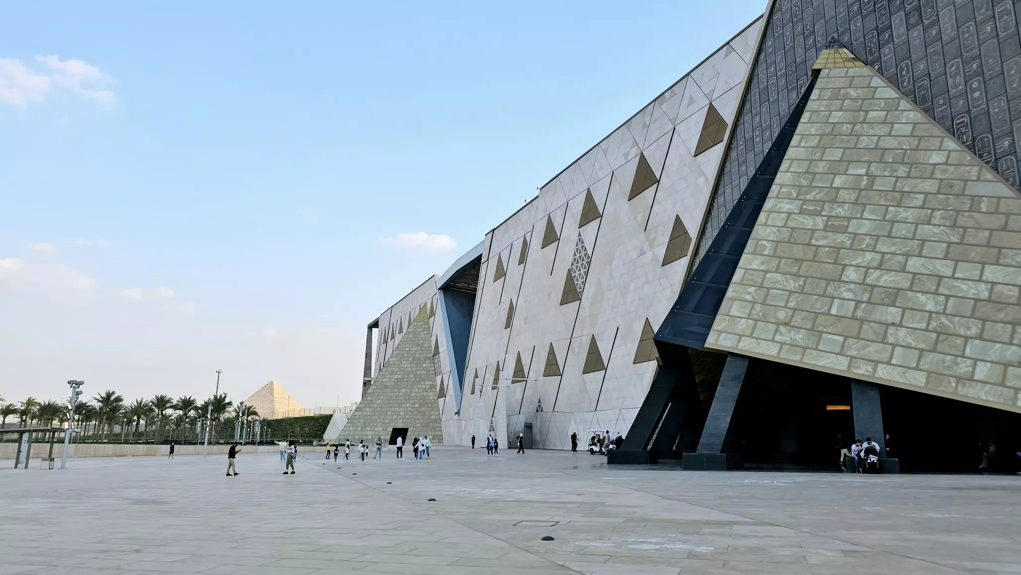 Exterior of a large museum complex with pyramid motifs as part of its architecture. In the distance stands a large pyramid.