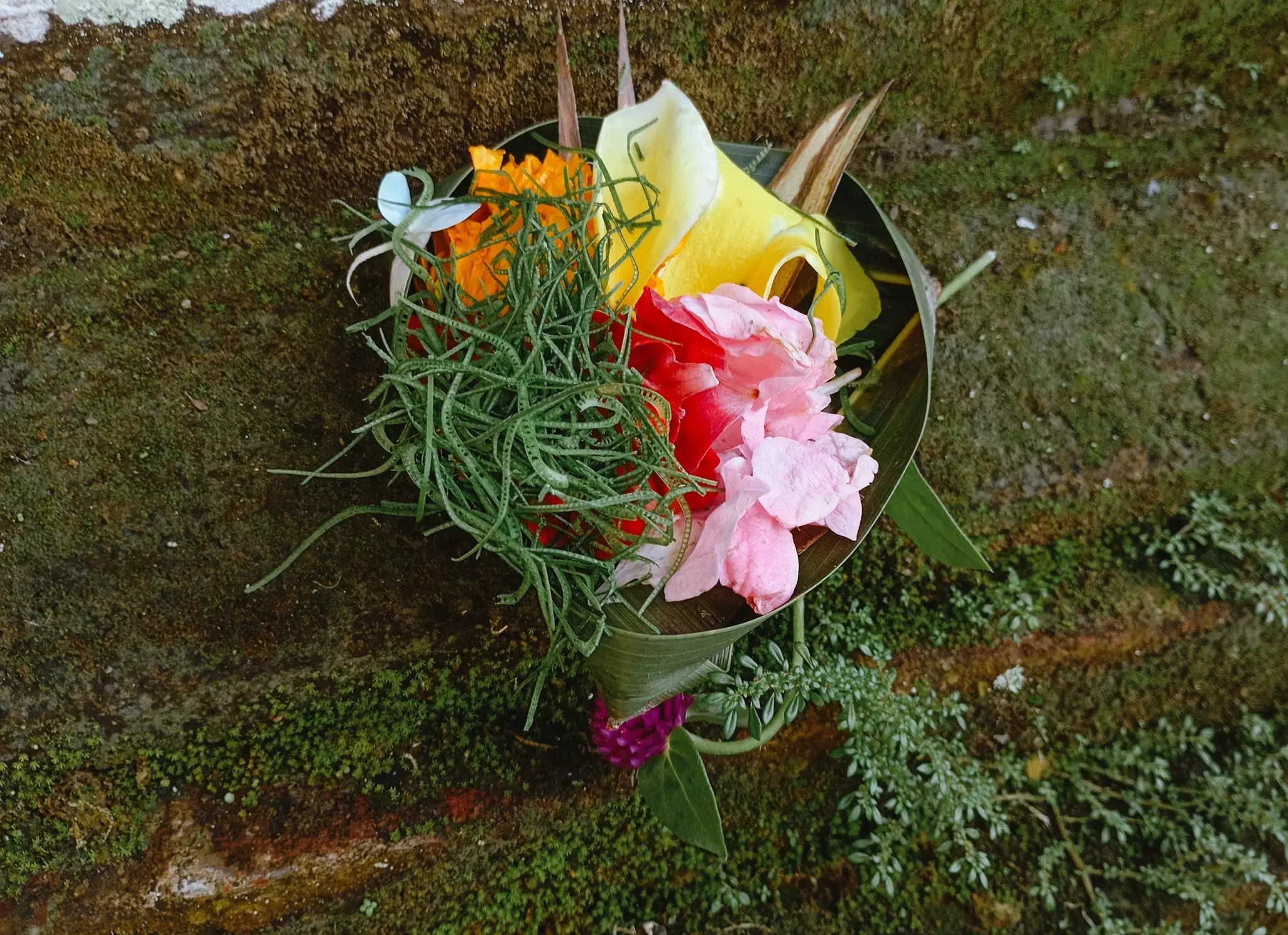 A small woven basket made of palm leaves and filled with flowers, rice, and incense.