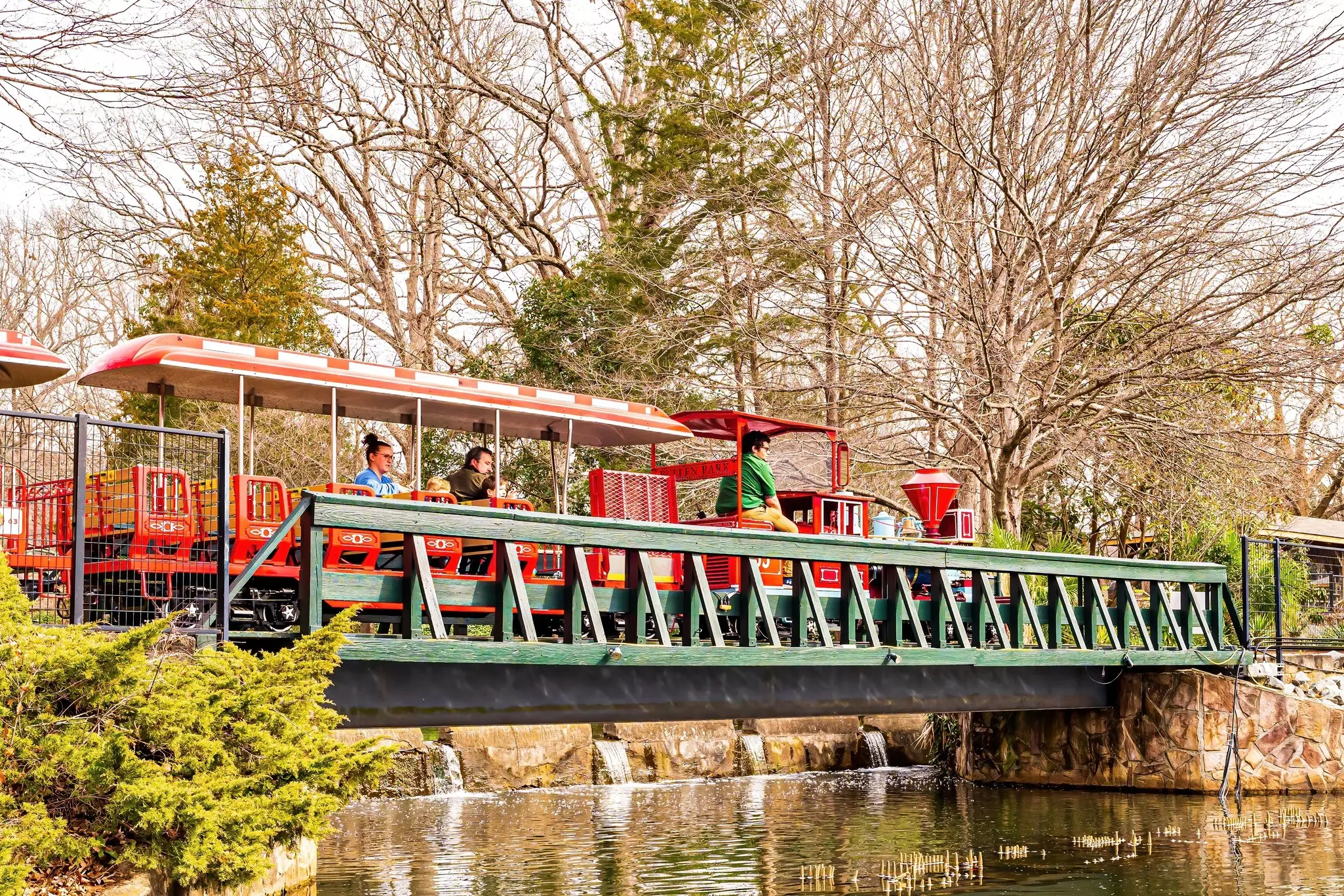 A red tourist train crosses a green bridge over water