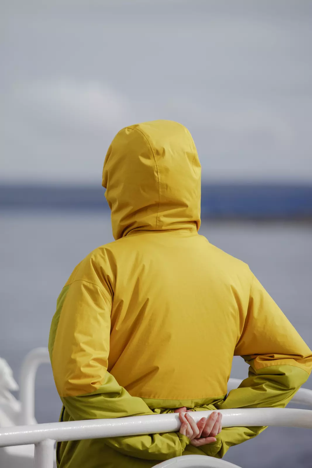 A person in a yellow waterproof jacket stands on a ferry.