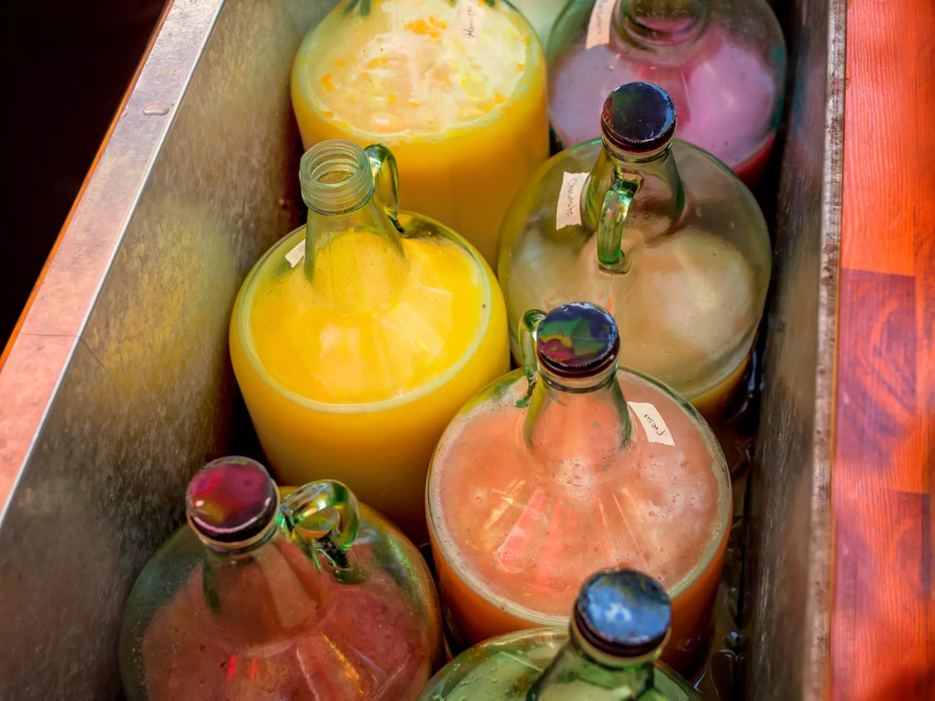 A red metal trough with colored liquid in clear glass jugs.