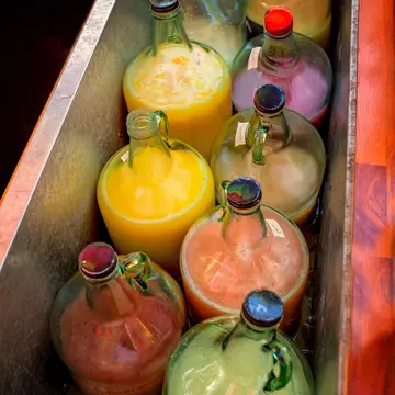 A red metal trough with colored liquid in clear glass jugs.