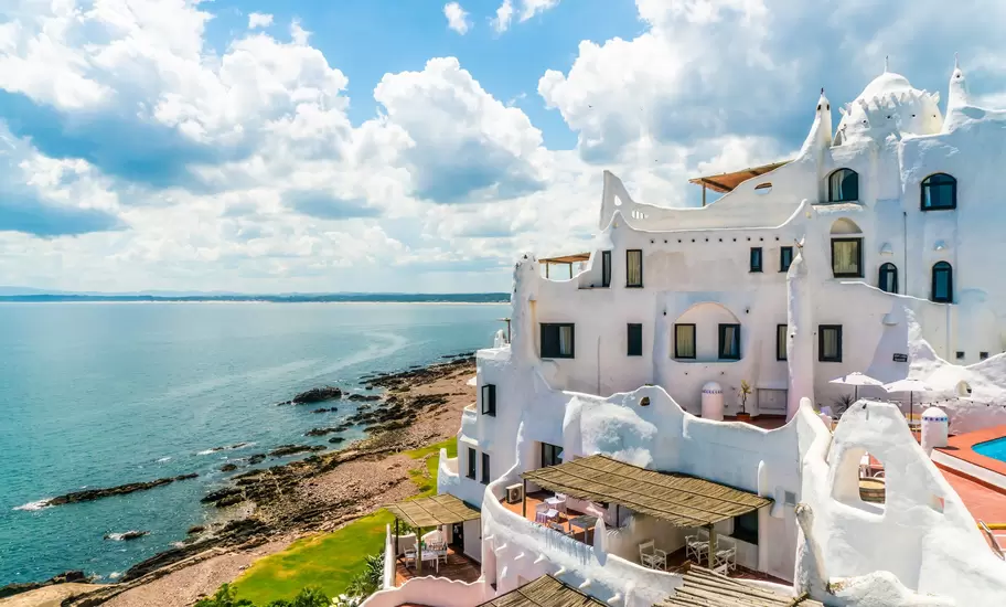 Casapueblo, a white sculpted building with domes and terraces on the rocky coast at Punta Ballena, Uruguay, above a calm sea